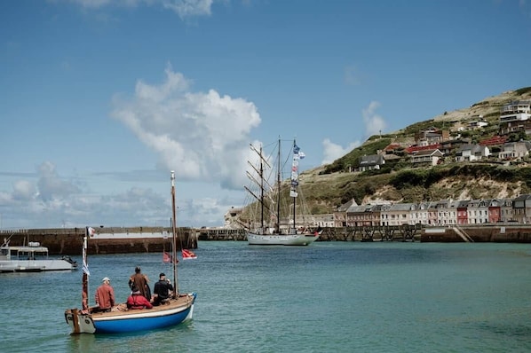 Un pueblo costero con un puerto, un barco de vela y edificios a lo largo de la colina.