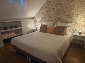 Un dormitori amb un llit gran, un armari, una tauleta de nit amb una làmpada i una paret amb un disseny floral.