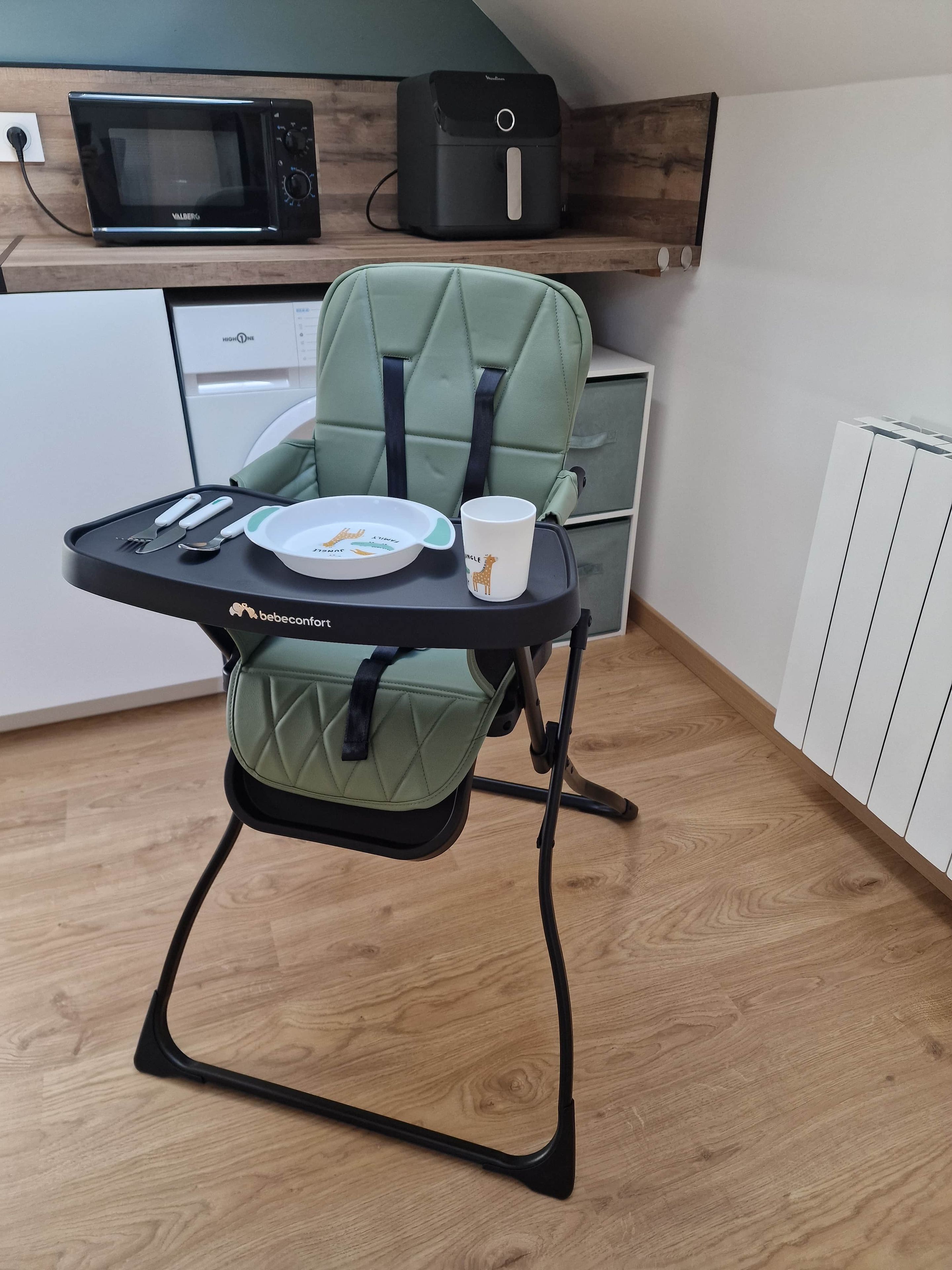 Een kinderstoel met een bekleed plateau, een beker en een bord met bestek.