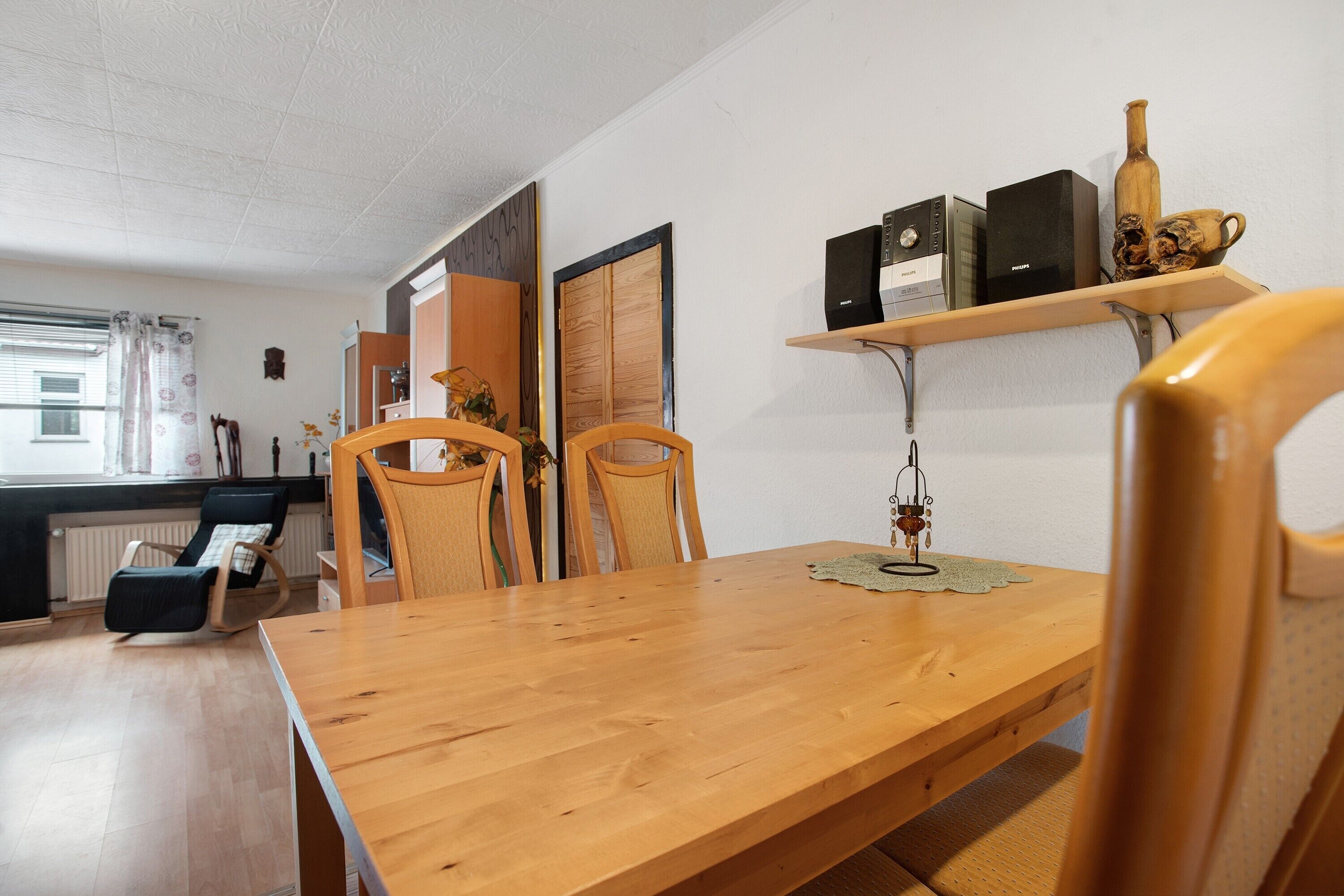 Ein Essbereich mit einem Holztisch und Stühlen, einer kleinen Ablage mit Kisten und einer Vase, sowie einem Heizkörper im Hintergrund.