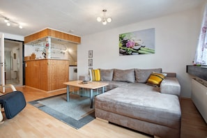 Ein modernes Wohnzimmer mit einer Couch, einem kleinen Tisch und einer Küchenzeile mit Holzschränken.