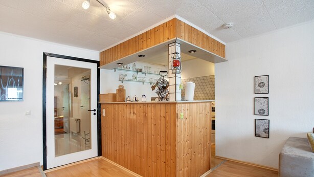 A wooden partition with a glass door, a shelf with glassware, and framed artwork on the wall.