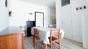 Ein Essbereich mit Tisch und Stühlen, eine Küche im Hintergrund und eine weiße Tür.