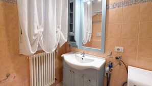 Un baño con un lavabo blanco, un espejo azul, un perchero para toallas y una ducha.