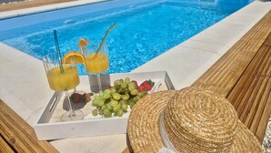 Cenário à beira da piscina com bandeja de bebidas, frutas e chapéu de palha.