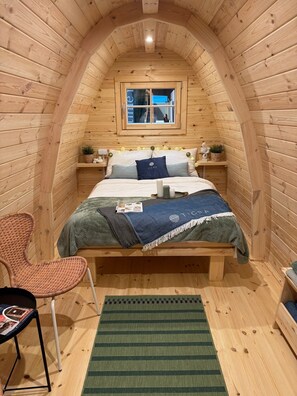 A cozy, wooden-paneled room with a bed, a chair, a small table, and a window. - Camp Diekirch - Camping Pod (Erpeldange-sur-Sûre)