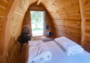 Une petite pièce chaleureuse aux murs en bois, avec un lit recouvert de draps blancs, une chaise et une petite table.