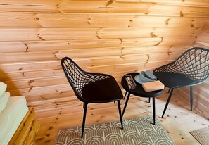 L’intérieur d’un chalet en bois, avec deux chaises à l’assise en tissu noir, une petite table et un tapis à motifs.