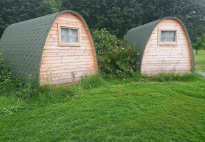 Deux structures en bois en forme de dôme, dotées de fenêtres, entourées d’herbe et d’arbres.