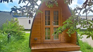 Una cabaña de madera con puerta principal, terraza de madera y un pequeño porche.