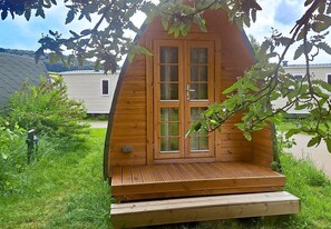 Une cabane en bois avec une porte d’entrée, une terrasse en bois et un petit porche.