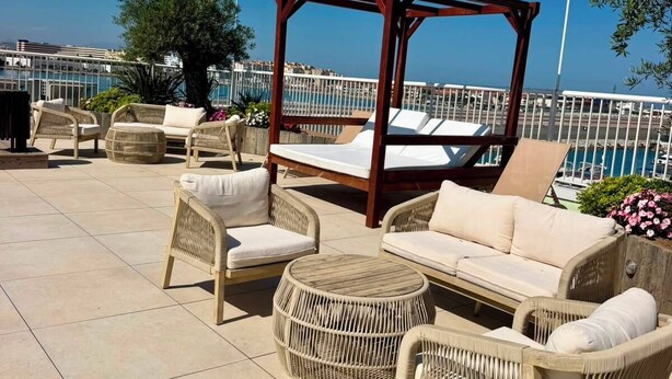 Una terraza en la azotea con muebles de mimbre, un toldo de madera y vistas al mar.