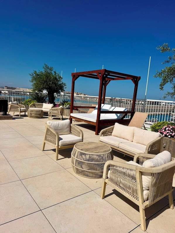 A rooftop terrace with wicker furniture, a wooden canopy, and a view of the sea. - Marina Club Luxury Apartment & Spa Resort (Gibraltar)