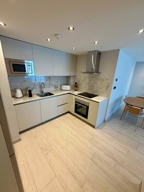 A modern kitchen with built-in appliances, a marble backsplash, and a wooden floor. - Marina Club Luxury Apartment & Spa Resort (Gibraltar)