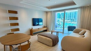 Una sala de estar moderna con una mesa de comedor de madera, un sofá, un televisor y un ventanal con vistas a la ciudad.