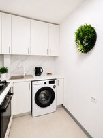 Una cocina compacta con armarios blancos, lavadora integrada, un lavabo y una cafetera.