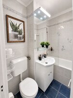 Un baño moderno con inodoro, lavamanos y ducha. En la pared, hay un cuadro con plantas.