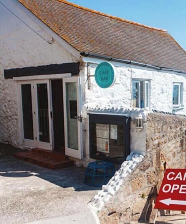 A white building with a cafe sign, a door, and a sign indicating the cafe is open.