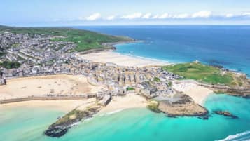 Vista aérea de un pueblo costero con playa, una estructura fortificada y una combinación de edificios residenciales y comerciales.