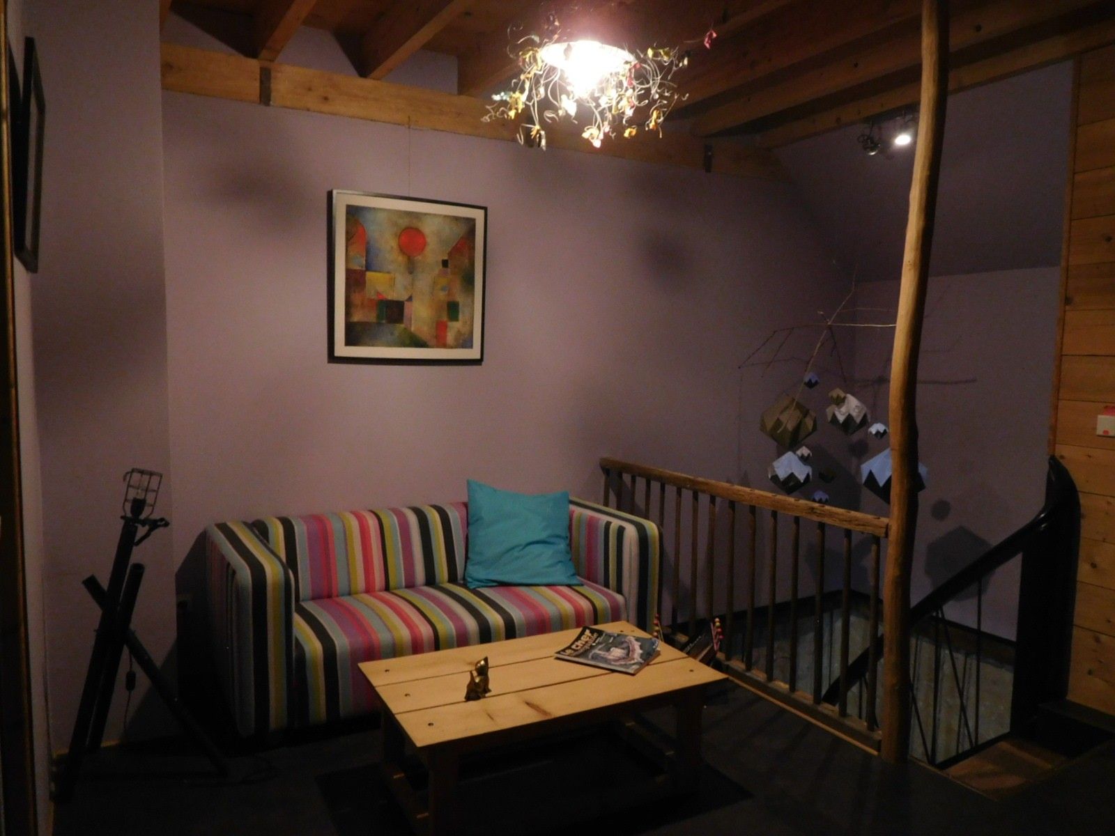 Une pièce avec un plafond en bois, un canapé rayé aux couleurs vives, une petite table avec un magazine et un tableau accroché au mur.