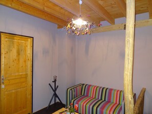 Et værelse med dør i træ, en farverig stribet sofa, en tripod lampe og en træbjælke i loftet.
