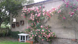 Un mur de jardin orné de rosiers grimpants, une petite table blanche et des pots en terre cuite.