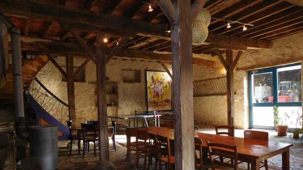 Un coin repas rustique avec des tables et des chaises en bois, un escalier et une grande fenêtre.