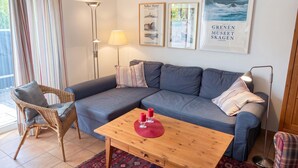 A living room with a sofa, a wooden coffee table, a wicker chair, a floor lamp, and a patterned rug. - FeWo Frische Brise - Lauterbach (Putbus)