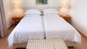 A double bed with white linens, two bedside tables with lamps, a woven bench, and a painting on the wall. - FeWo Frische Brise - Lauterbach (Putbus)