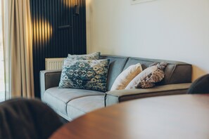 Una sala de estar moderna con un sofá, cojines estampados, un radiador y una pared oscura.