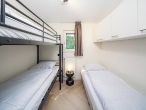 Habitación compacta con literas, una mesita de noche pequeña, ventana con cortinas y un radiador.