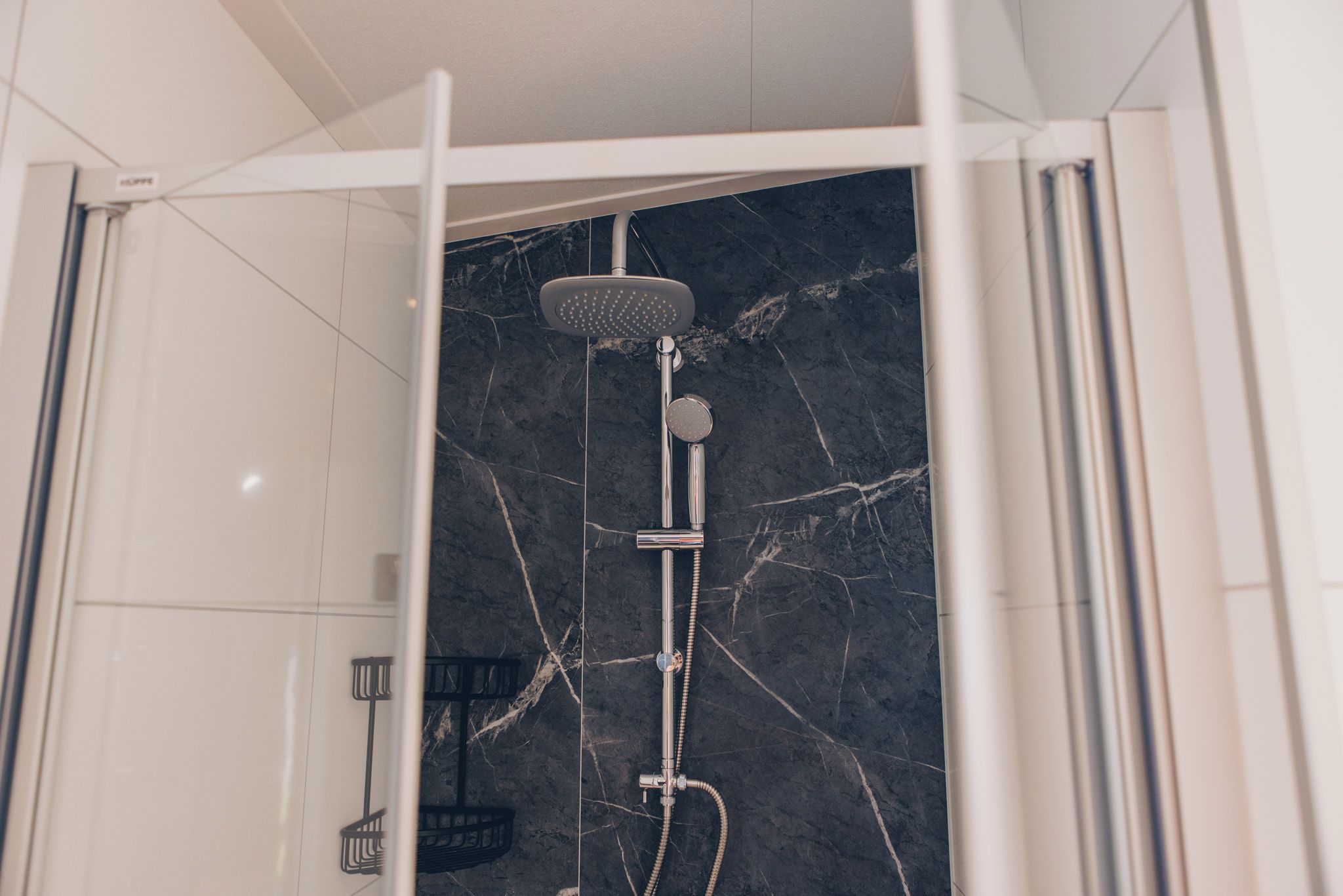A shower with a marble wall, a handheld showerhead, and a control knob.