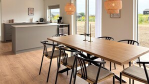 A modern kitchen with a central island, a dining area with a wooden table and chairs, and large windows offering a view of the outdoors. - 4 bedroom cozy home in Haderslev (Haderslev)