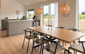 Eine moderne Küche mit einer zentralen Kochinsel, einem Essbereich mit Holztisch und -stühlen und großen Fenstern mit Blick ins Freie.
