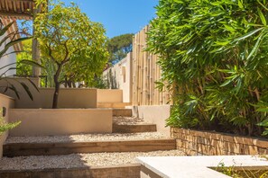 A courtyard with steps leading to a seating area, surrounded by greenery and a bamboo fence.