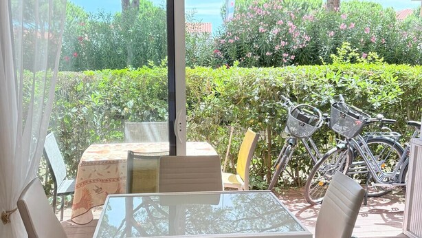 En terrasse med et glasbord og stole, udsigt til grønt og cykler udenfor.