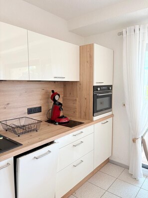 Eine moderne Küche mit weißen Schränken, einer Holz Arbeitsplatte, einer roten Kaffeemaschine und einem eingebauten Backofen.