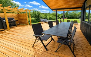 Eine Terrasse im Freien mit Holztisch und -stühlen, einer Pergola und einem Grillbereich.