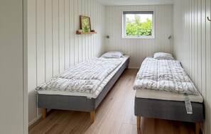 Ein Zimmer mit zwei Einzelbetten, einem Fenster mit Blick ins Grüne und einem Regal mit einem gerahmten Bild.