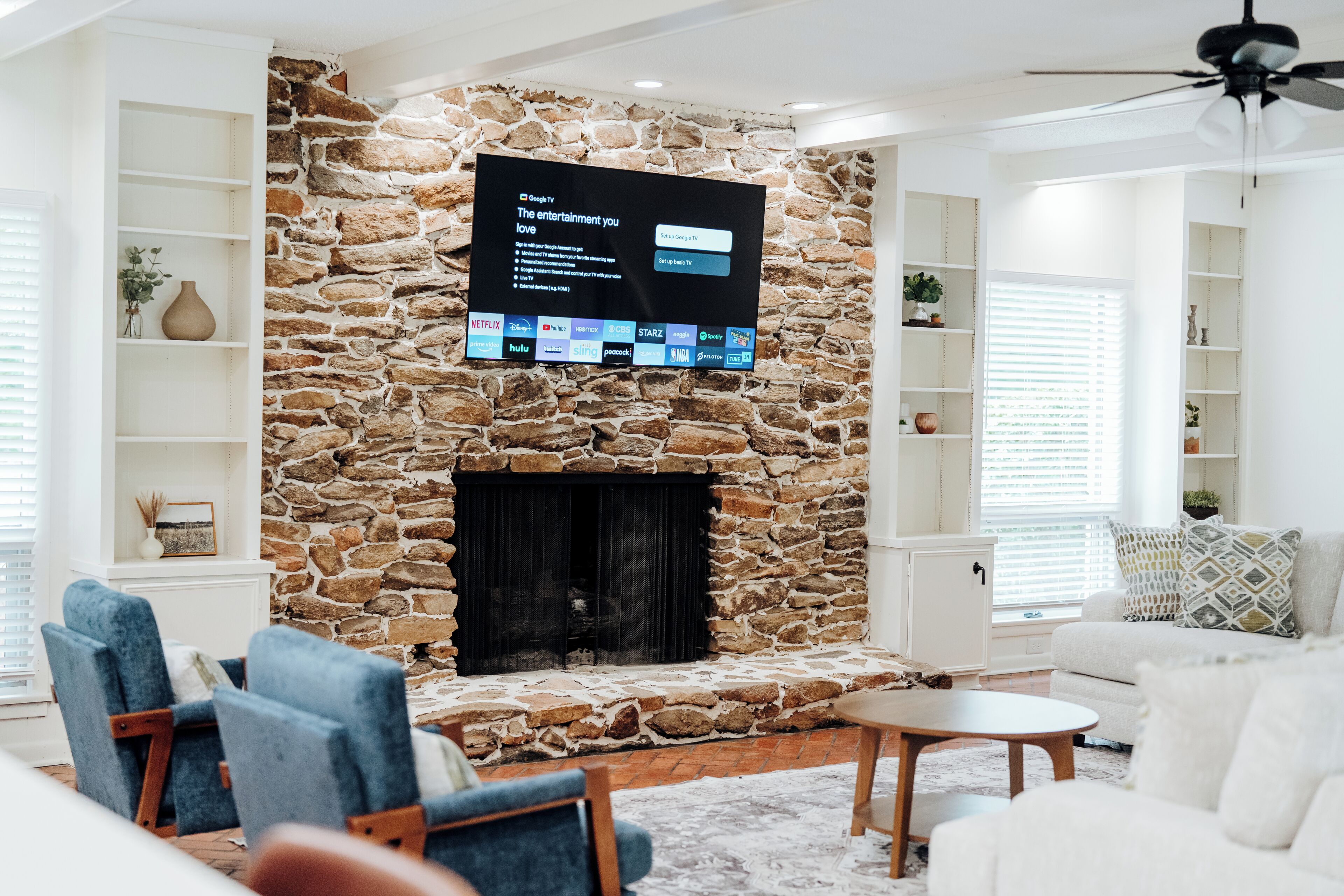 A living room with a stone fireplace, a flat-screen TV mounted on the wall, and seating arrangements.