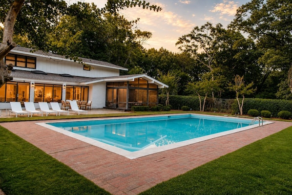 A modern house with a swimming pool, a patio with lounge chairs, and a well-maintained garden.