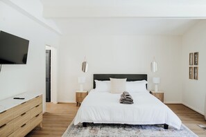 Ein Schlafzimmer mit einem Bett, Nachttischen, einem Fernseher und einer hölzernen Kommode.