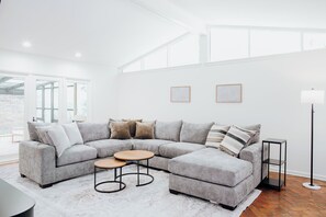 Ein modernes Wohnzimmer mit einem grauen Ecksofa, zwei runden Couchtischen, einer Stehlampe und gerahmten Kunstwerken an der Wand.