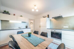 Uma cozinha moderna com armários brancos, uma mesa de jantar de madeira e um forno embutido.