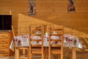 A wooden interior with a table set for four, wooden chairs, a television, and two posters on the wall. - Cozy Apartment Near the Slopes for 4 People (Orcières)