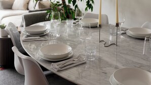 Een eettafel gedekt met borden, glazen en kaarsen, omringd door stoelen.