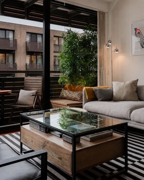 Ein modernes Wohnzimmer mit einem Glastisch, einer Couch, einem Sessel und einer großen Pflanze.