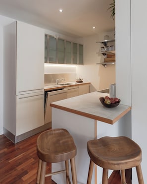 Eine moderne Küche mit weißen Schränken, einer Holz Arbeitsplatte und zwei hölzernen Barhocker.
