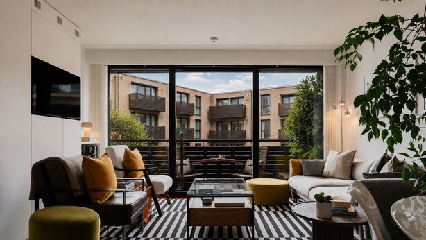 Een moderne woonkamer met een zwart-wit gestreept tapijt, een bank, een bijzettafeltje en uitzicht op een bakstenen gebouw door grote ramen.