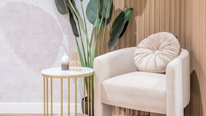 A room with a white chair, a round gold table, and a large green plant. - Apartamentos Príncipe de Canalejas (Ma)